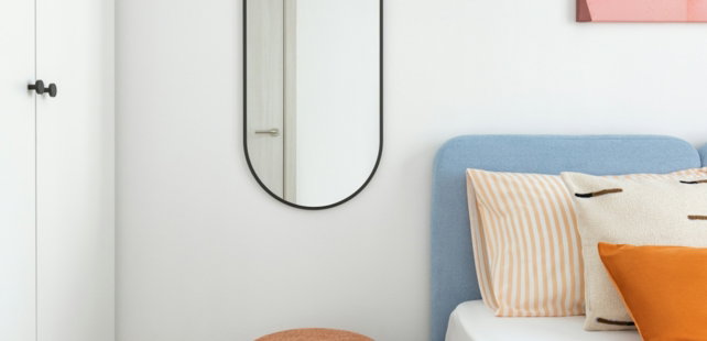 A minimalist bedroom with a blue bed and orange stool.